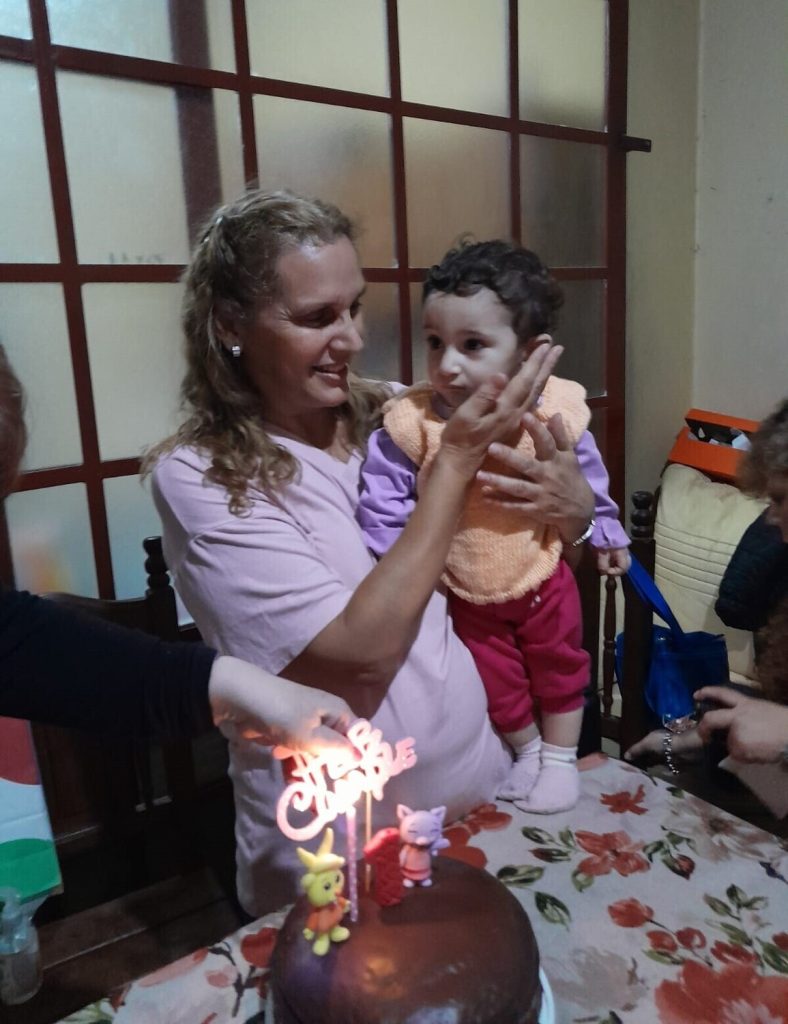 Gabriela sonriendo mientras sostiene en brazos a su hija Milagros junto a una torta de cumpleaños.