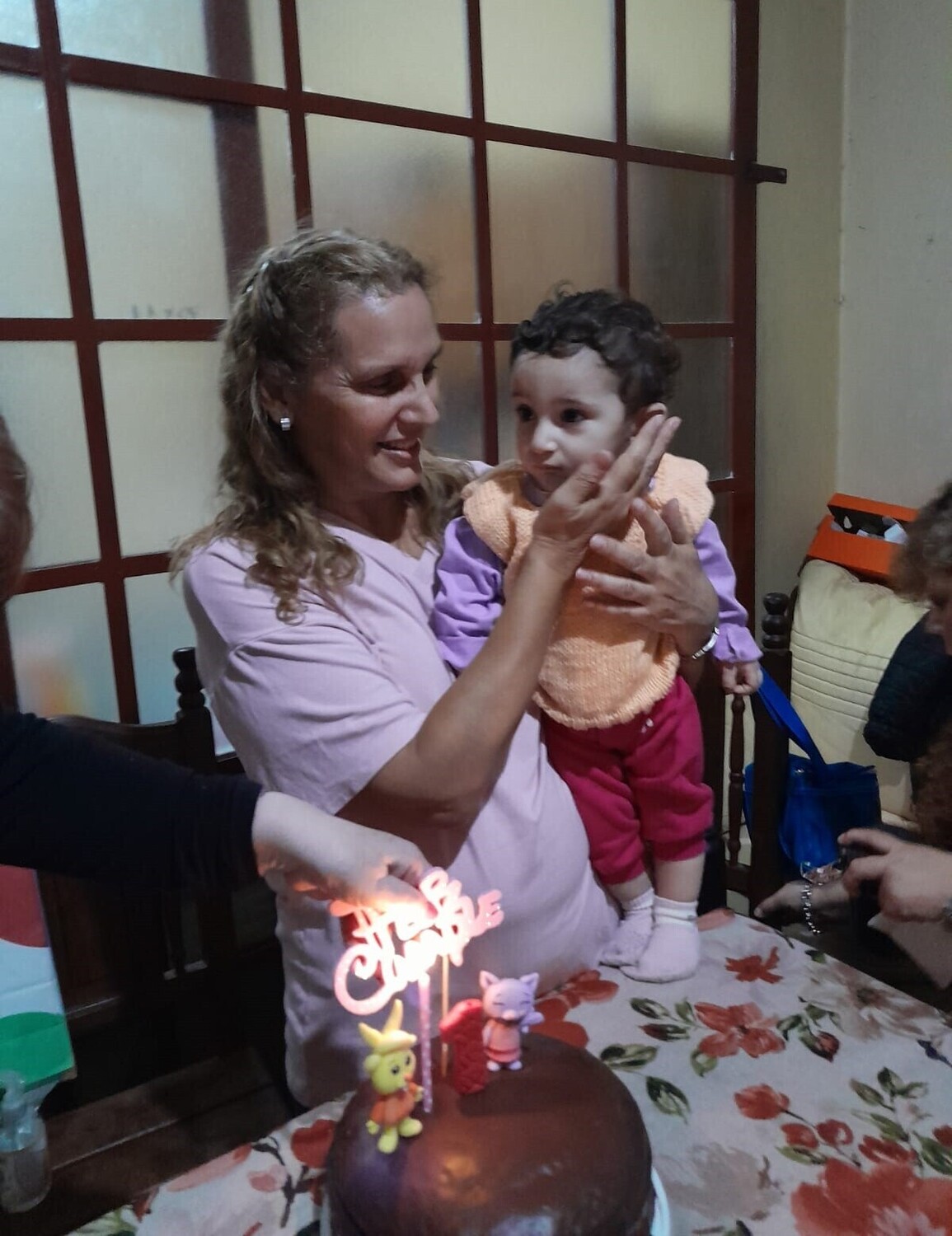 Gabriela sonriendo mientras sostiene en brazos a su hija Milagros junto a una torta de cumpleaños.