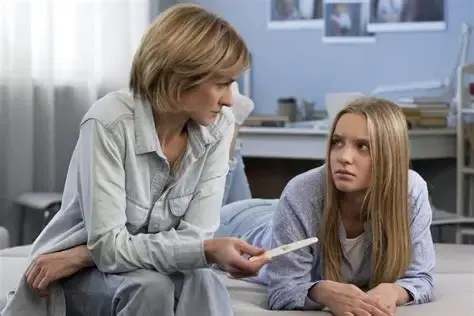 Una madre conversando con su hija adolescente sosteniendo una prueba de embarazo.