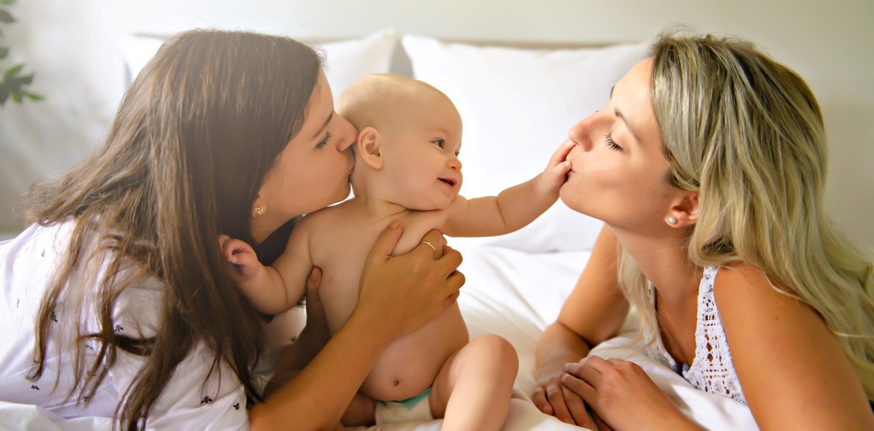 Pareja de dos mujeres en la cama jugando con su bebé.