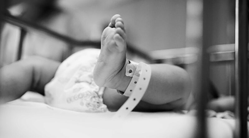 El pie de un bebé recién nacido con pulsera de identificación en una cuna hospitalaria, en blanco y negro
